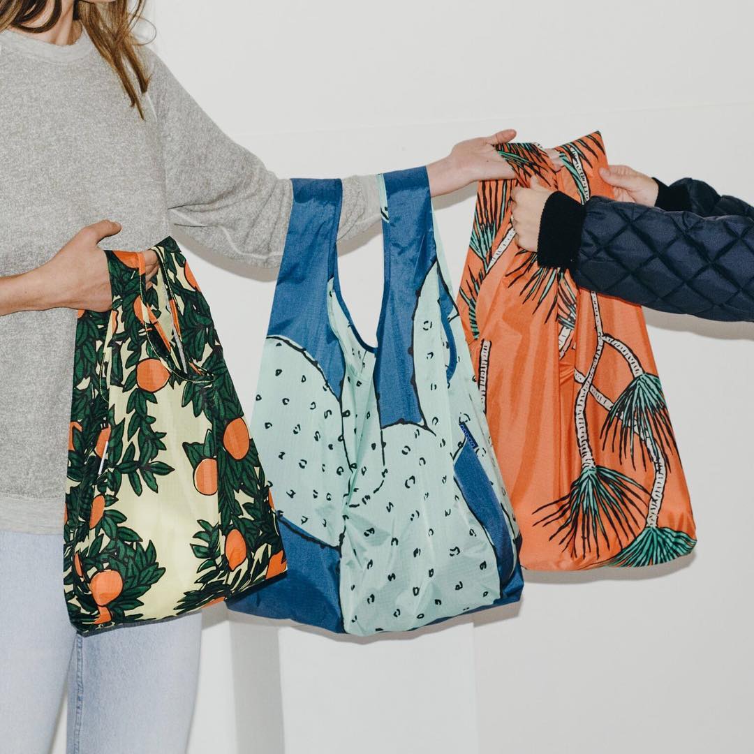 A model holds three baggu bags on her arms
