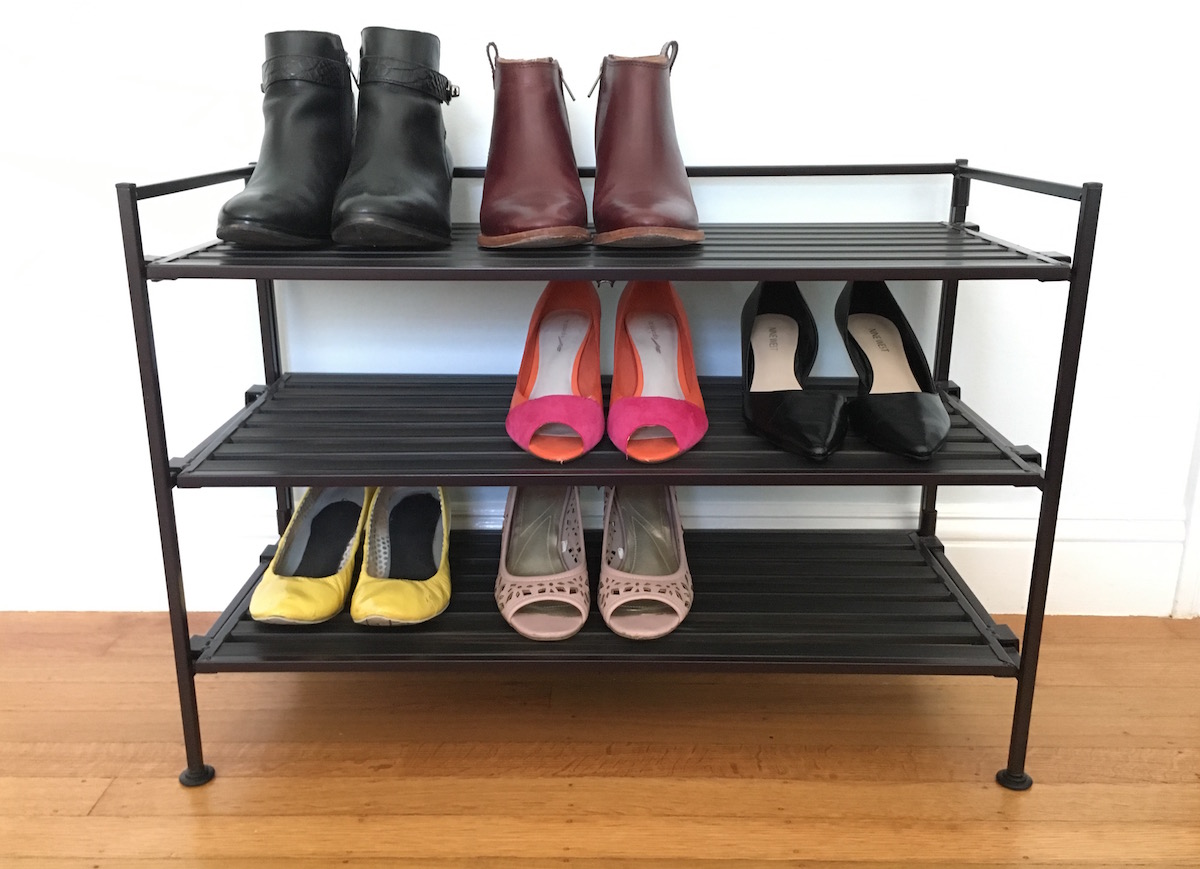 A shoe rack with three tiers, capable of holding about 9 pairs of shoes, with 6 pairs of shoes on it.