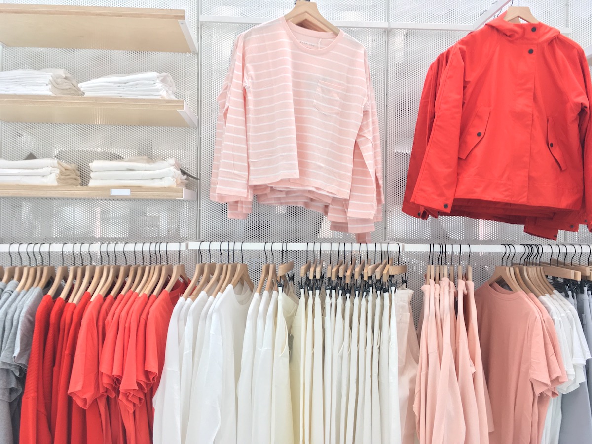 Racks and shelves of clothing at the Everlane store in San Francsico, showing pink, orange, and white clothing.