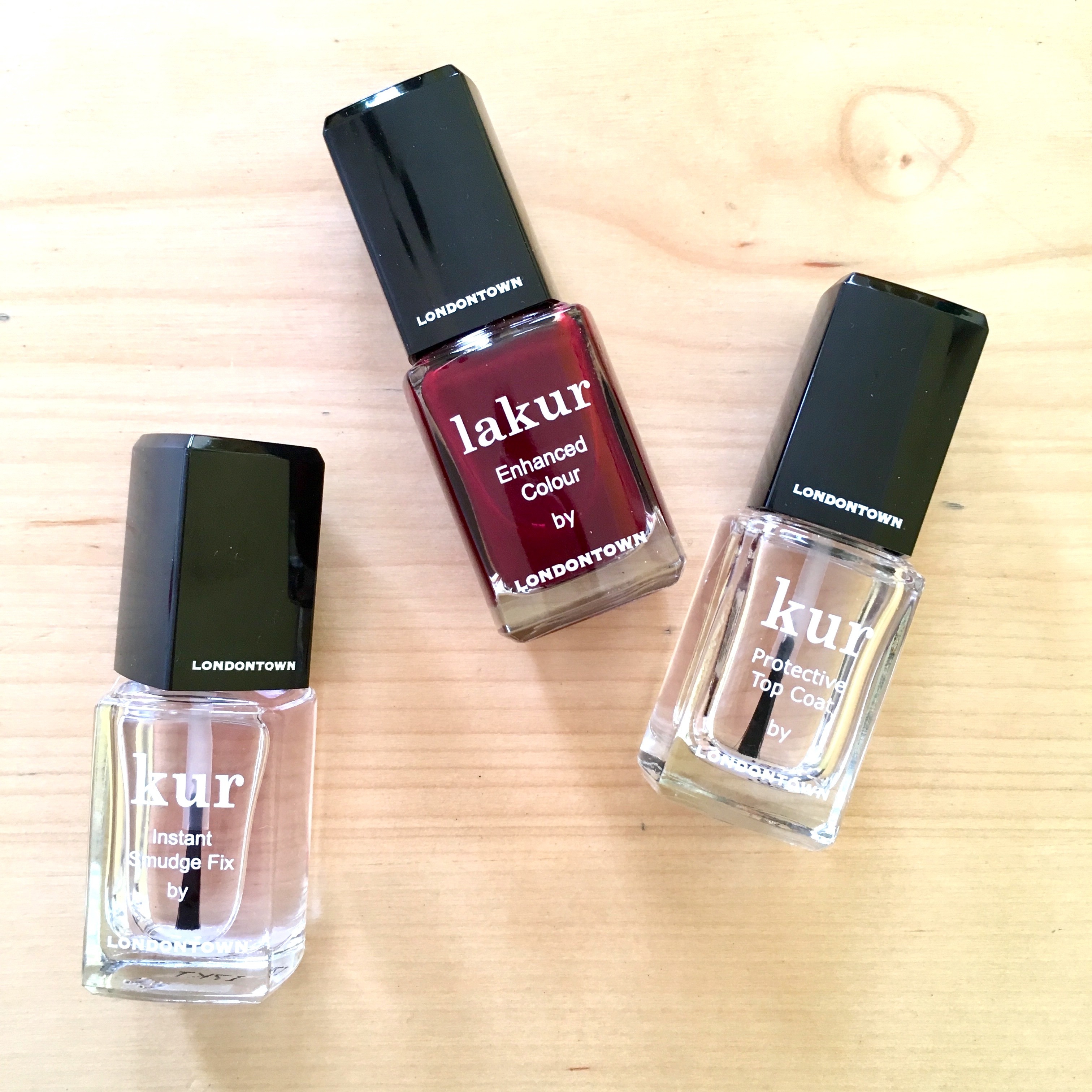 Three bottles of nail polish by Londontown lay flat on a light-colored wood table.