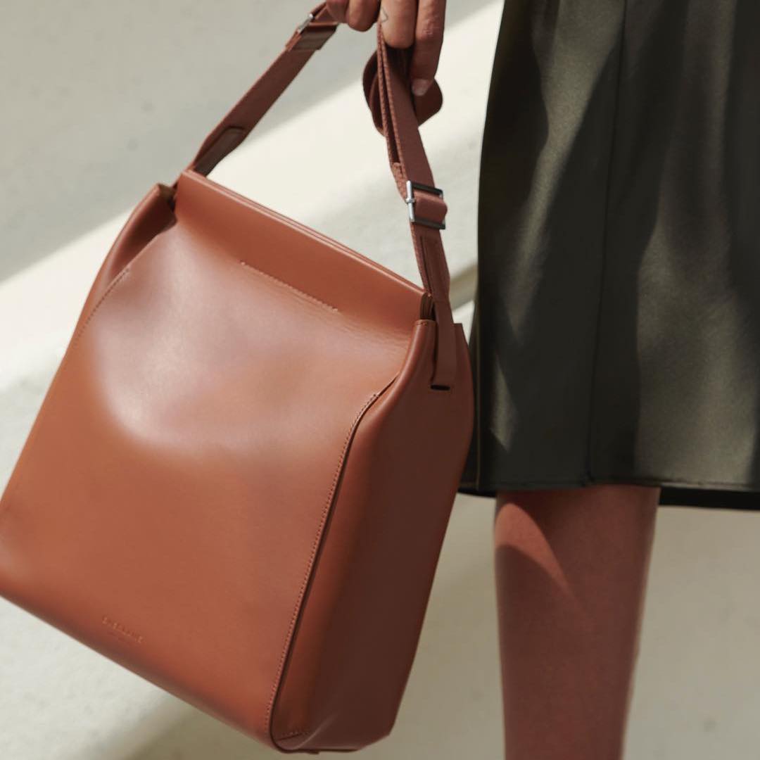 A hand holding a brown square-shaped leather bag.
