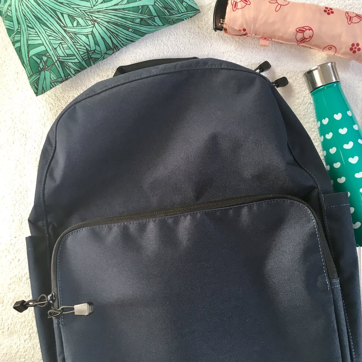Lo & Sons Backpack Review: a flat lay of a navy backpack with some items such as an umbrella and water bottle.