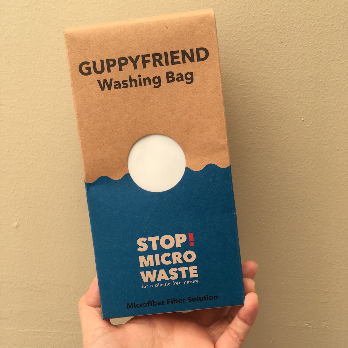 A hand holding a cardboard box for a Guppyfriend Washing bag.