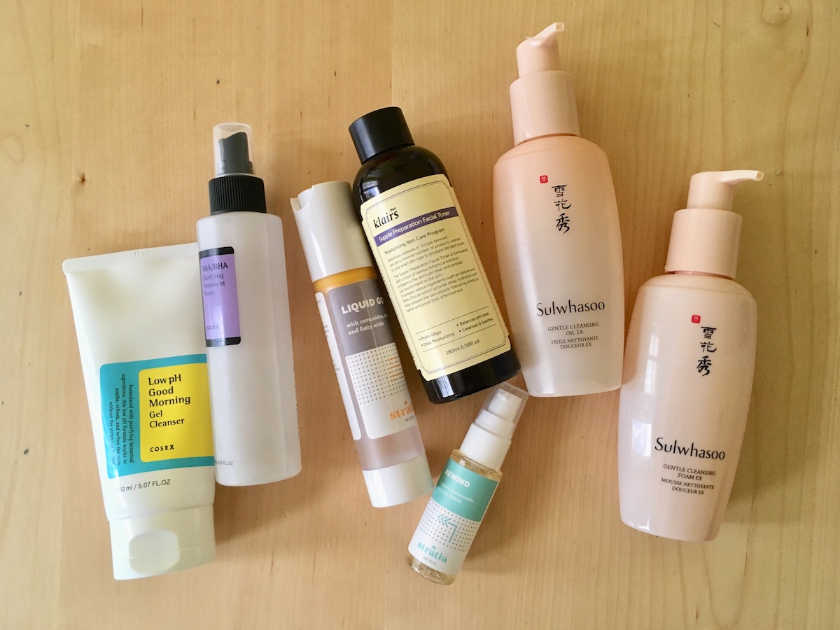 My Asian skincare routine: A variety of bottles on a wooden background, including products by Cosrx, Stratia Skin, Sulwhasoo, Klairs, and Elta MD.