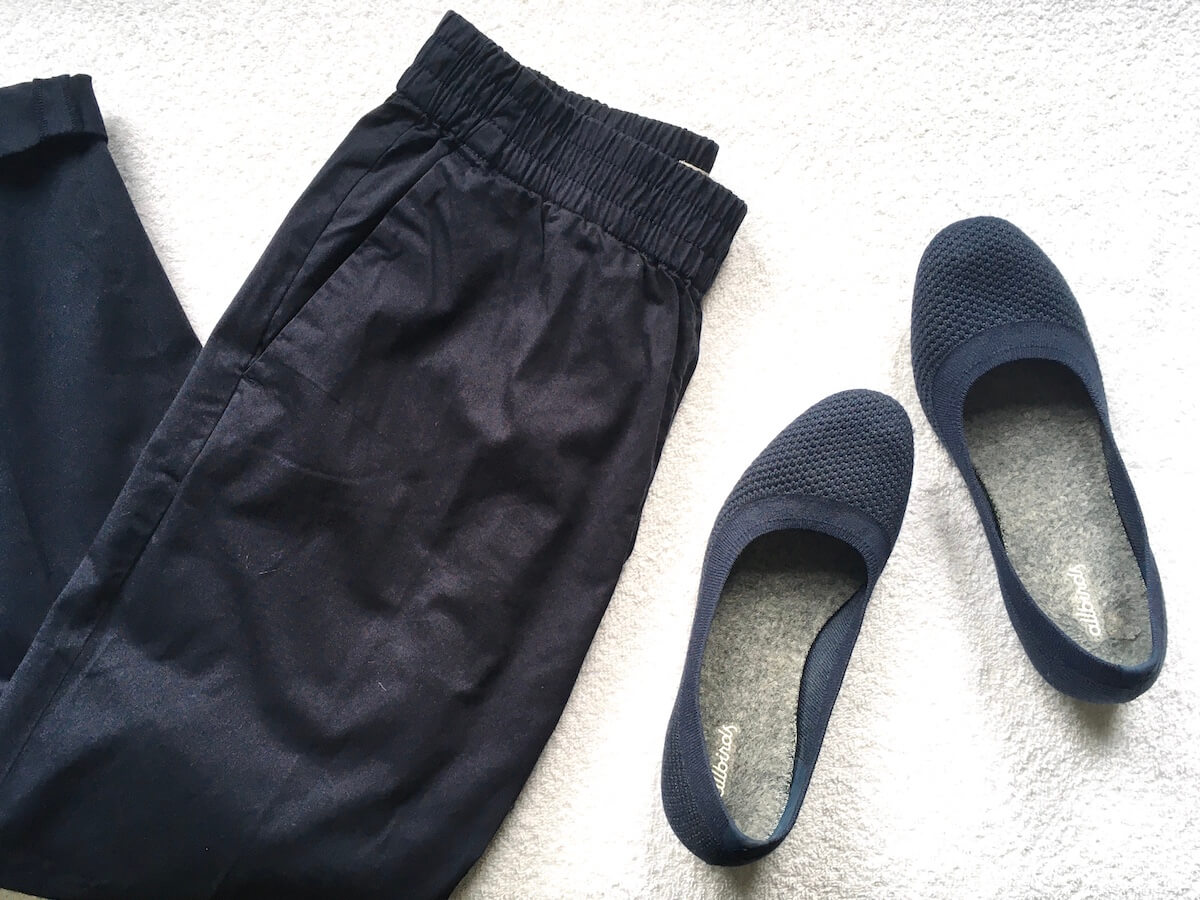 A flatlay of a pair of navy Everlane pants and blue Allbirds Tree Breezer flats.