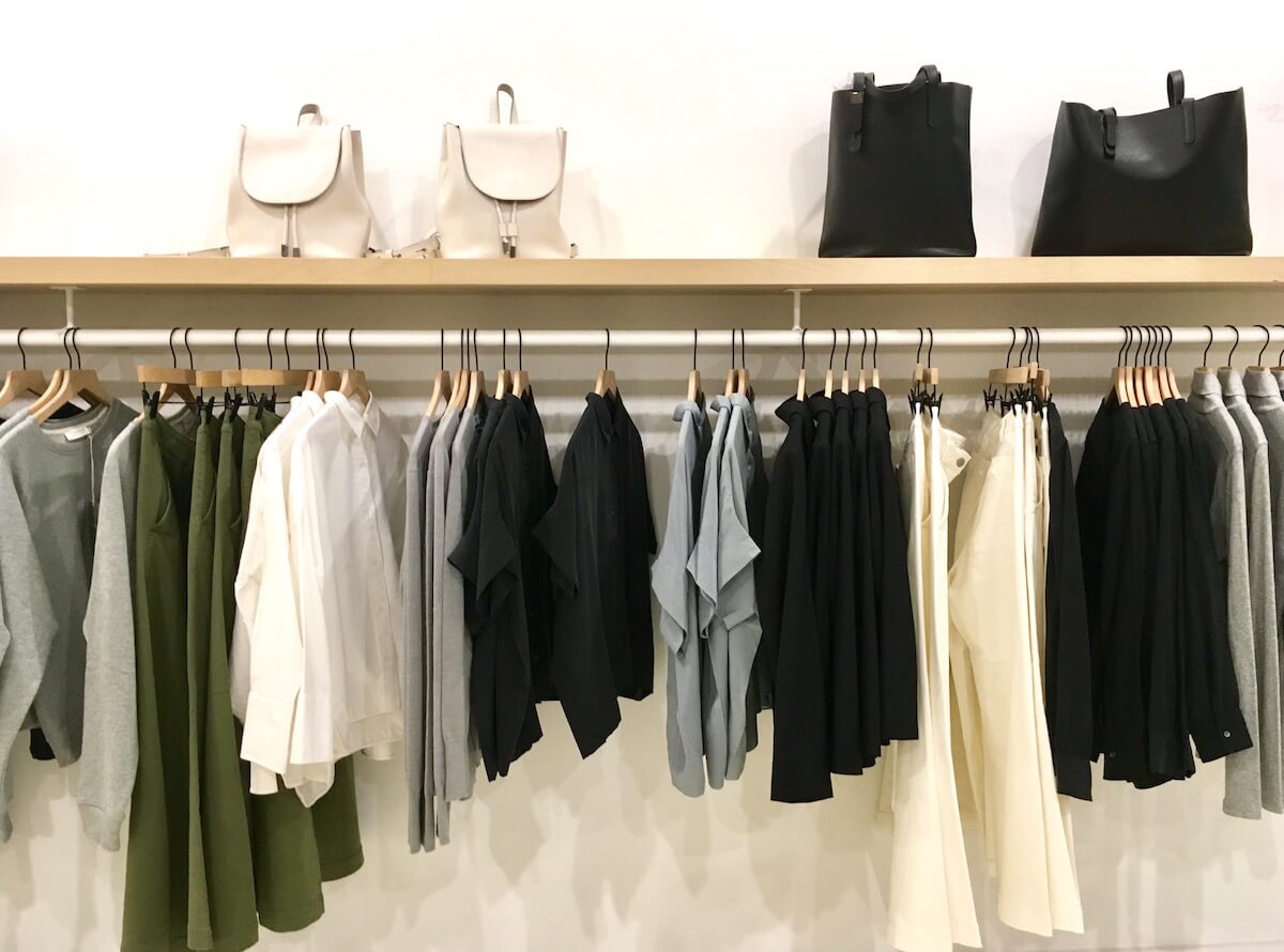 Everlane Reviews: A rack of clothing at Everlane. There is a shelf on top of the clothes rack, on which sits leather bags.