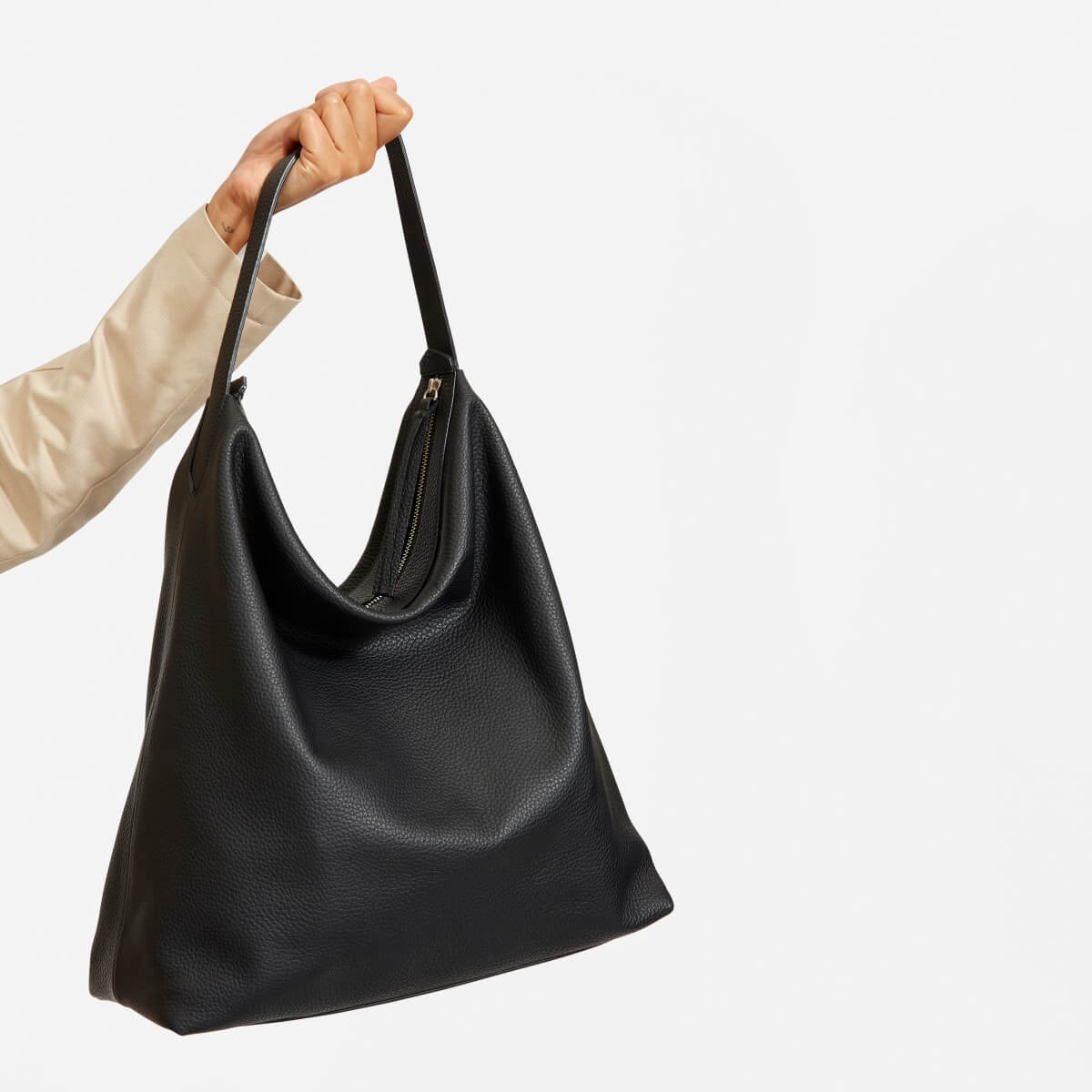 Everlane Boss Bag in black, a hobo leather bag, as held in someone's hand.