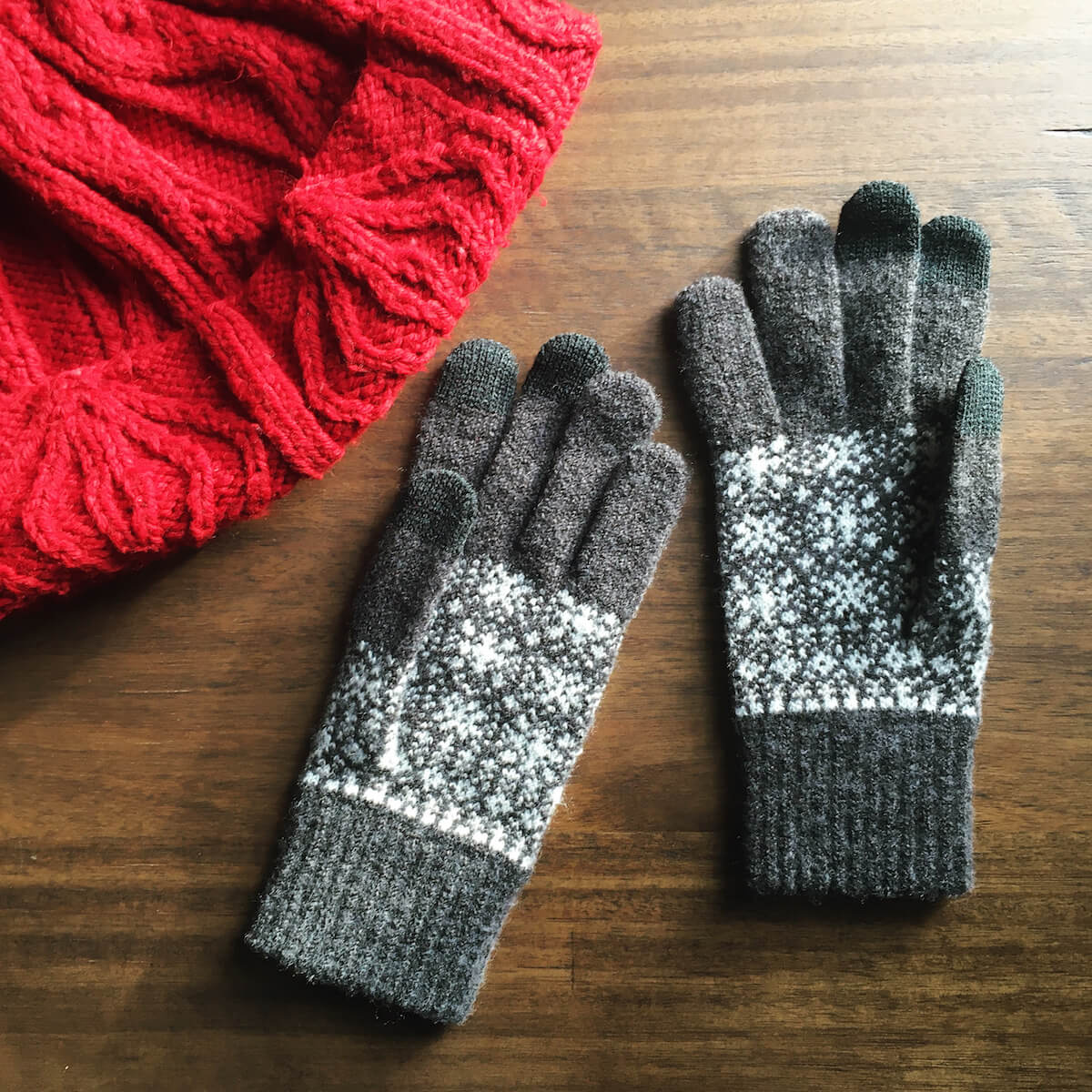 A pair of gray knit gloves with a snowflake pattern on a wood surface