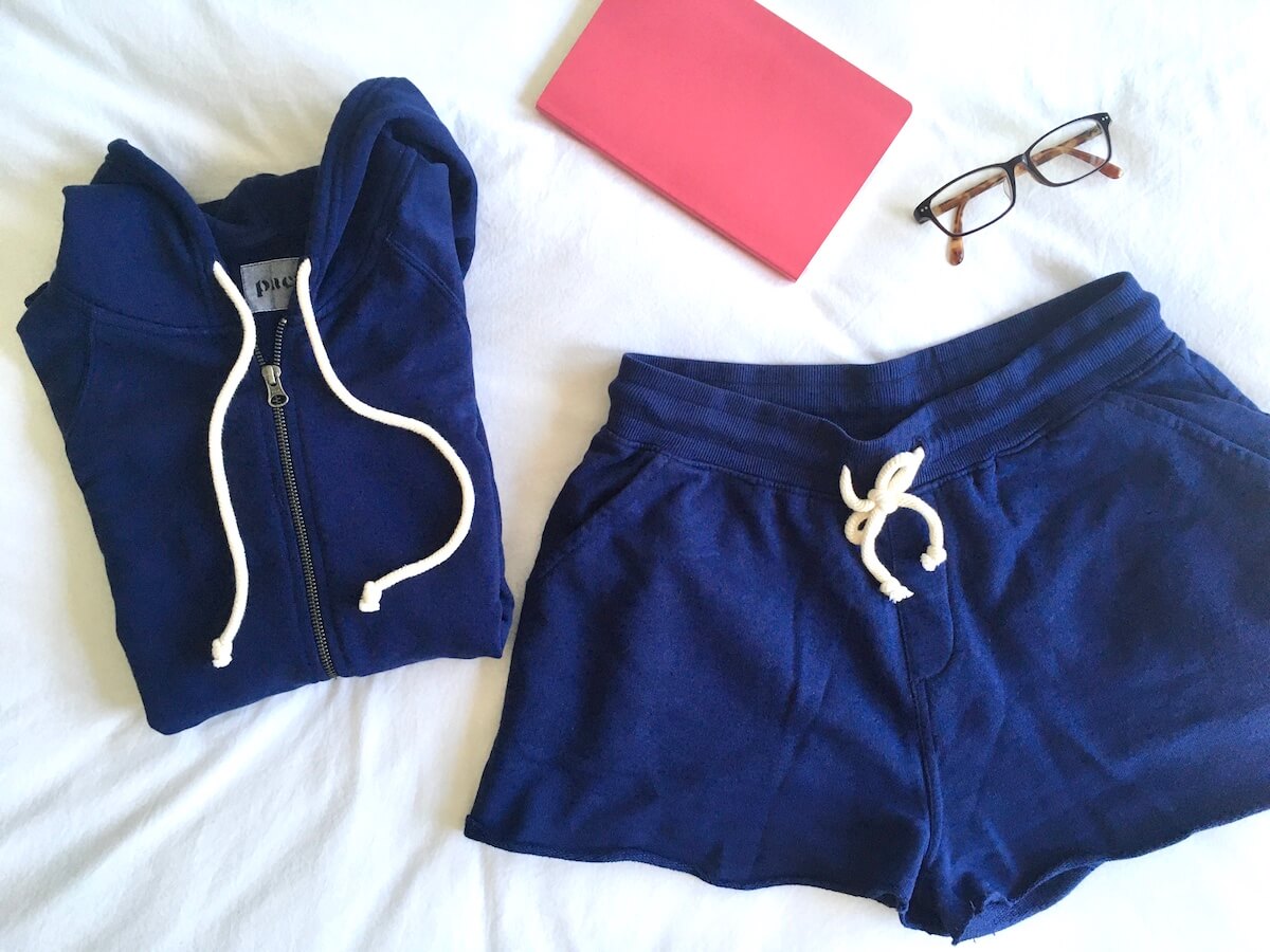 Pact Essential Hoodie and Drawstring short, flat lay style with glasses and a pink journal