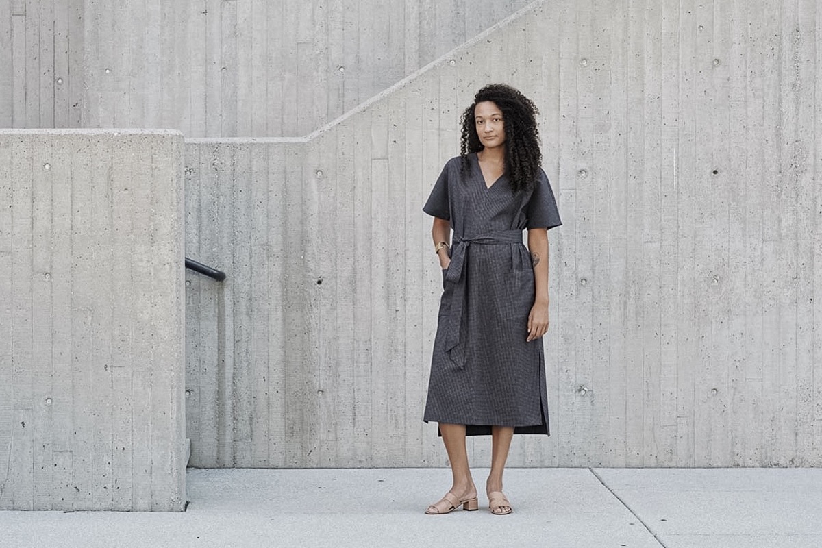 A Black model with curly hair wears a midi dress in front of a concrete wall