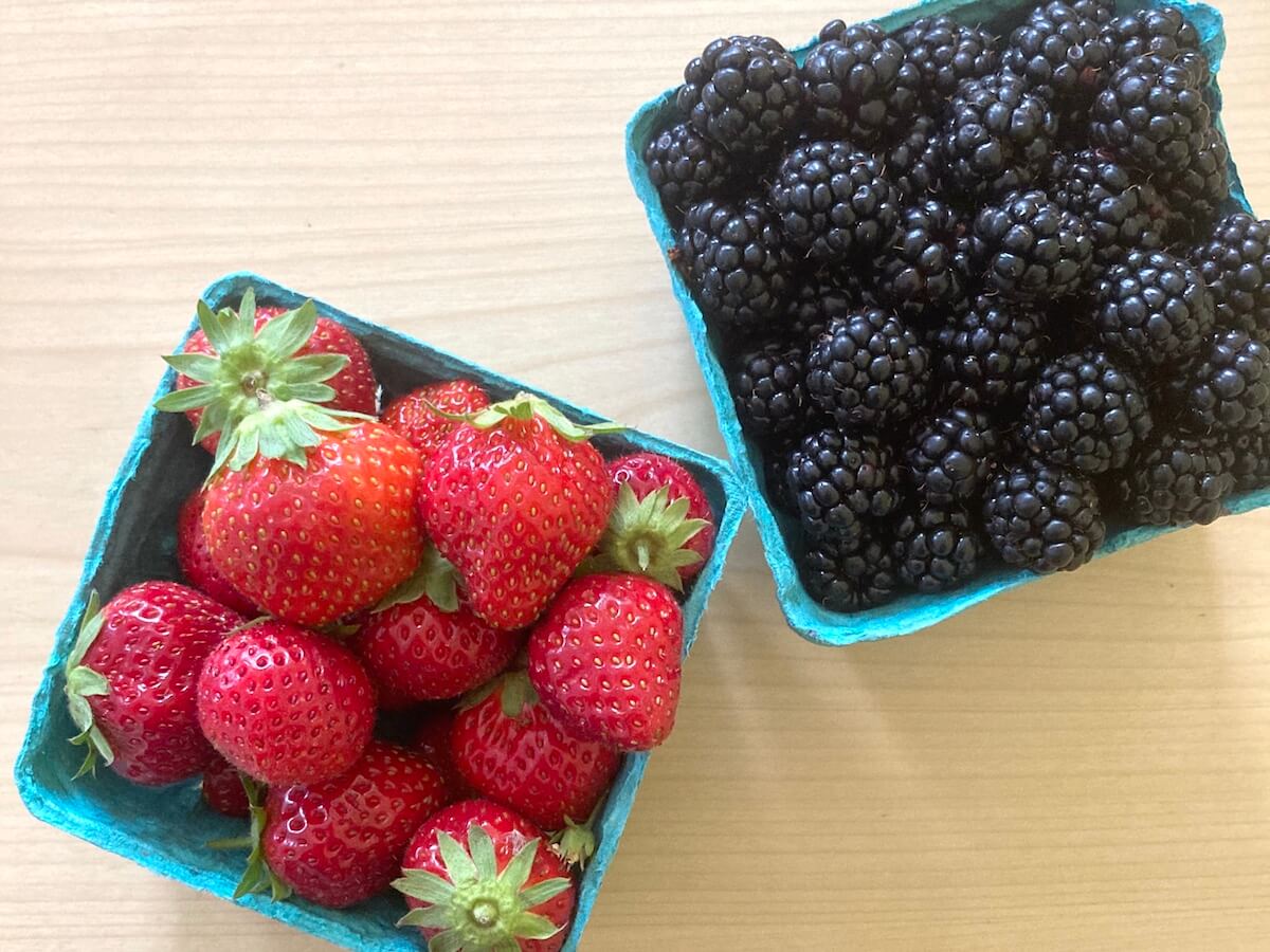 A basket of strawberries and blackberries in green cardboard containers