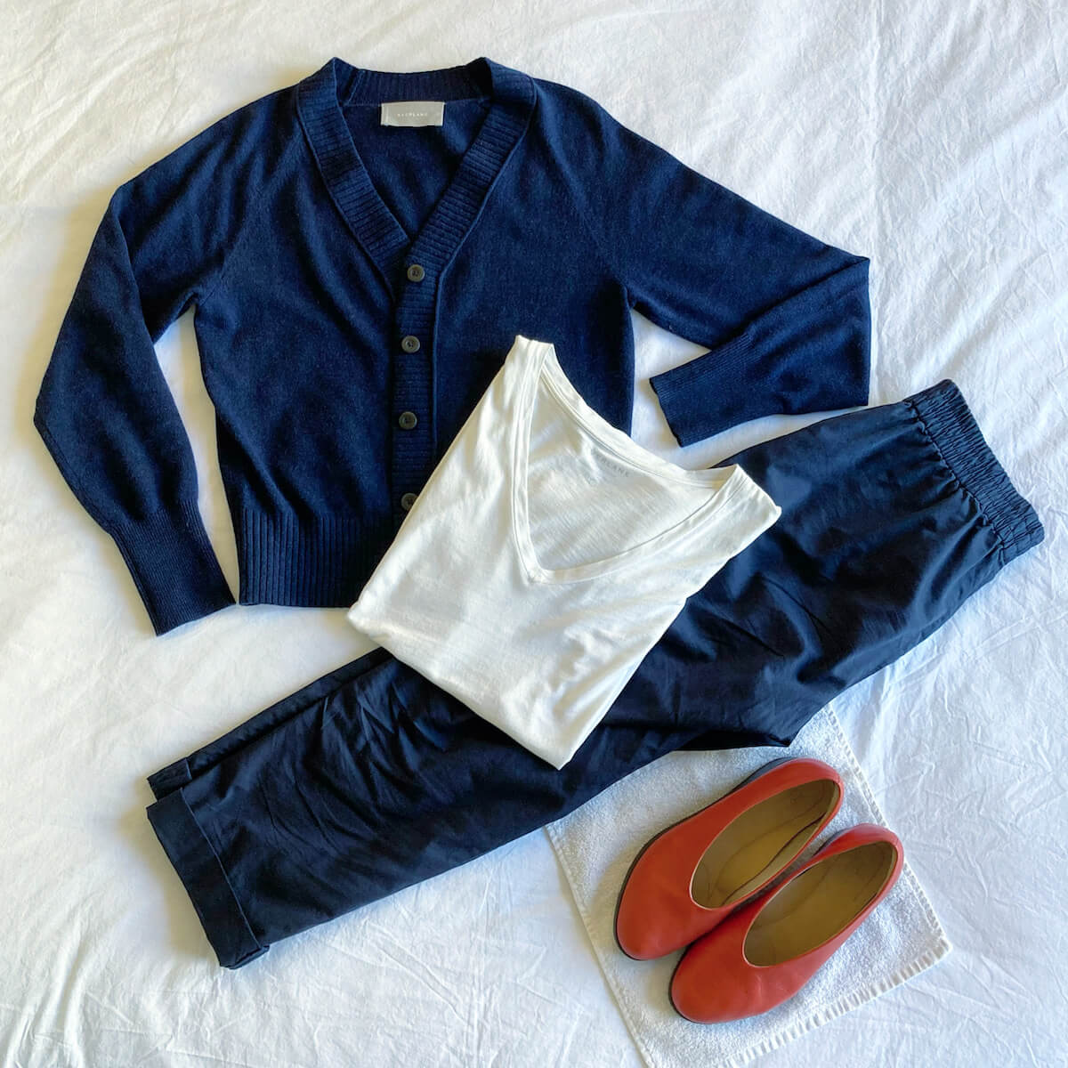 Flat lay of cardigan, navy pants, white t-shirt, and red shoes.