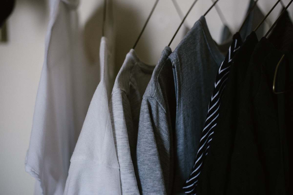 White, gray, and black shirts on hangers in a closet.