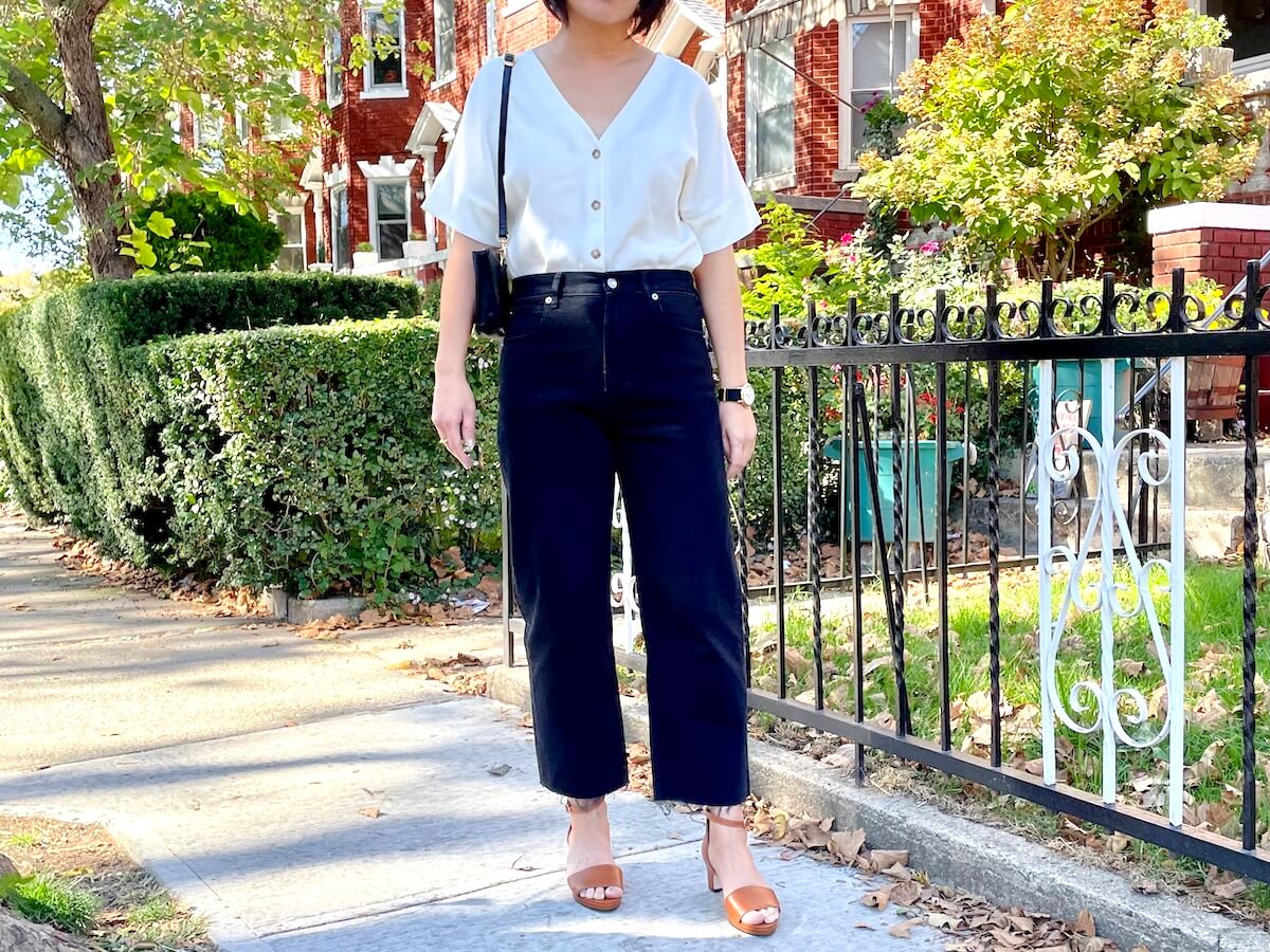 Me, a person with short black hair, standing outside wearing the Everlane Way-High Jean with sandals. There are red brick homes in the background.