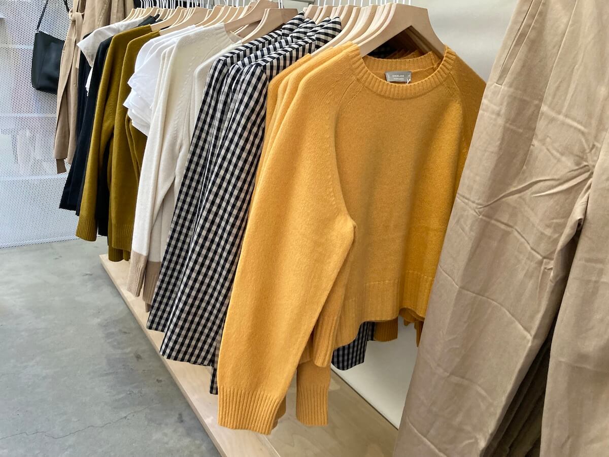 A rack of clothing in an Everlane store, with orange crewneck sweaters in front