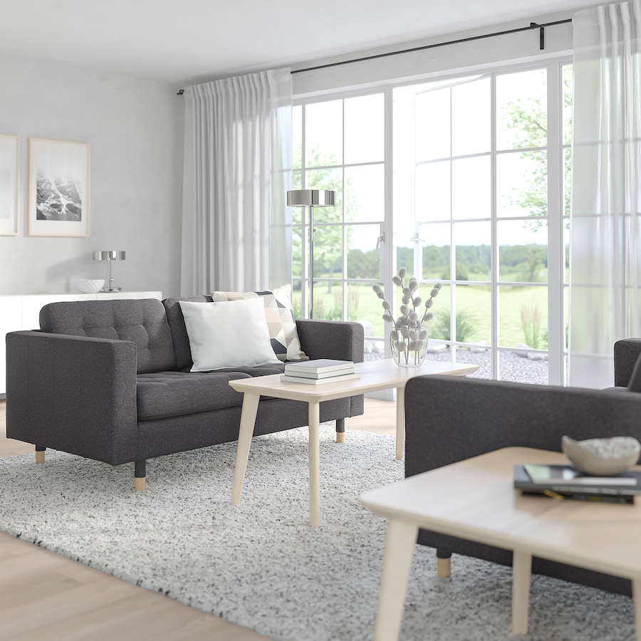 A gray loveseat with tufted cushions from Ikea in a white room with large windows.