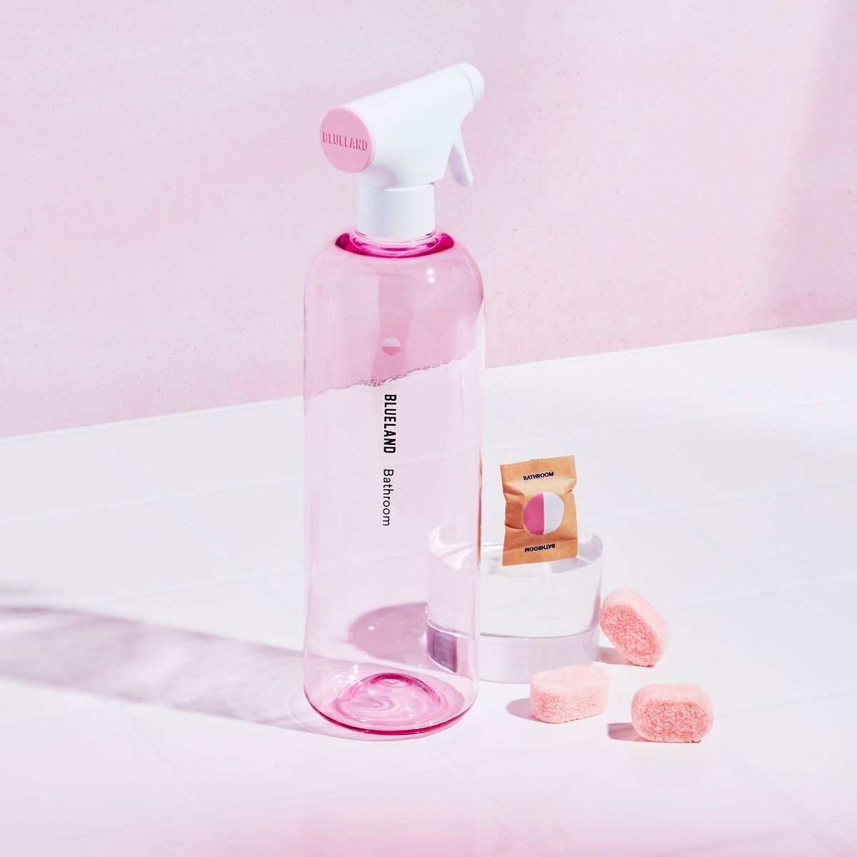 Blueland spray bottle and tablets on a counter with a pink background.