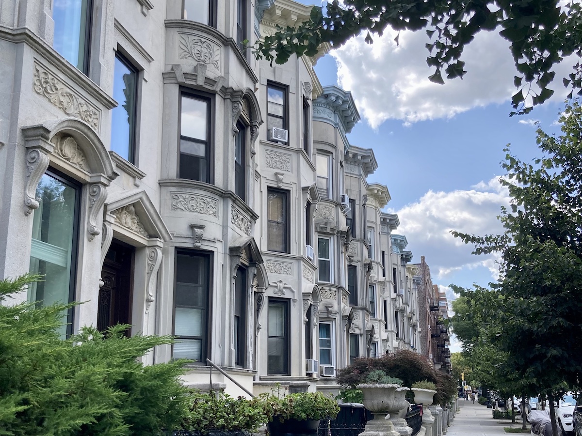 A row of brownstones in Brooklyn with blue skies and green trees.