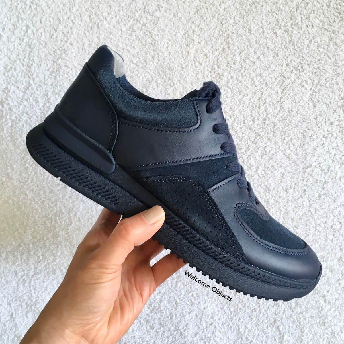 A hand holding up a navy blue Everlane trainer sneaker