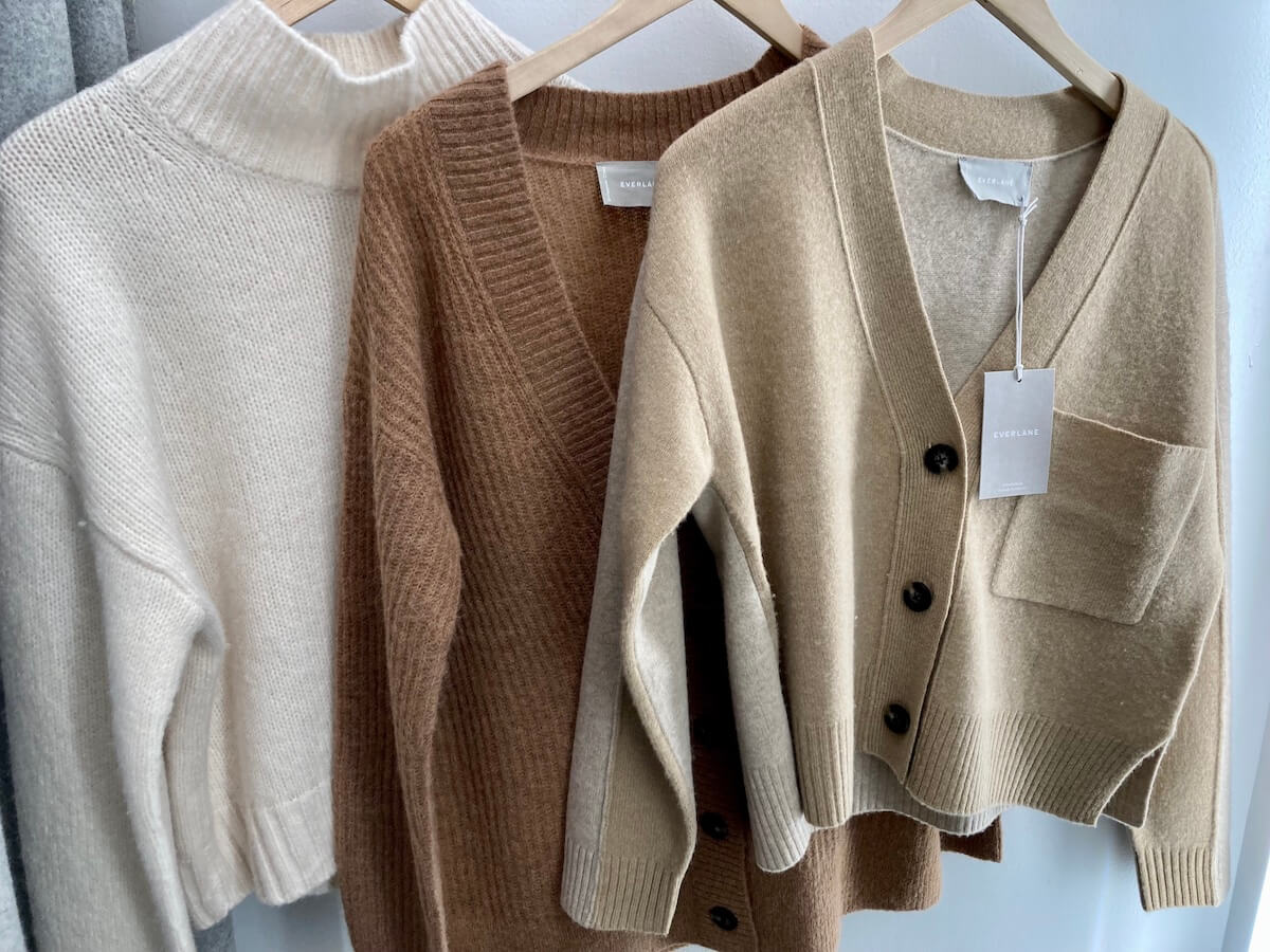 Three sweaters on wooden hangers.