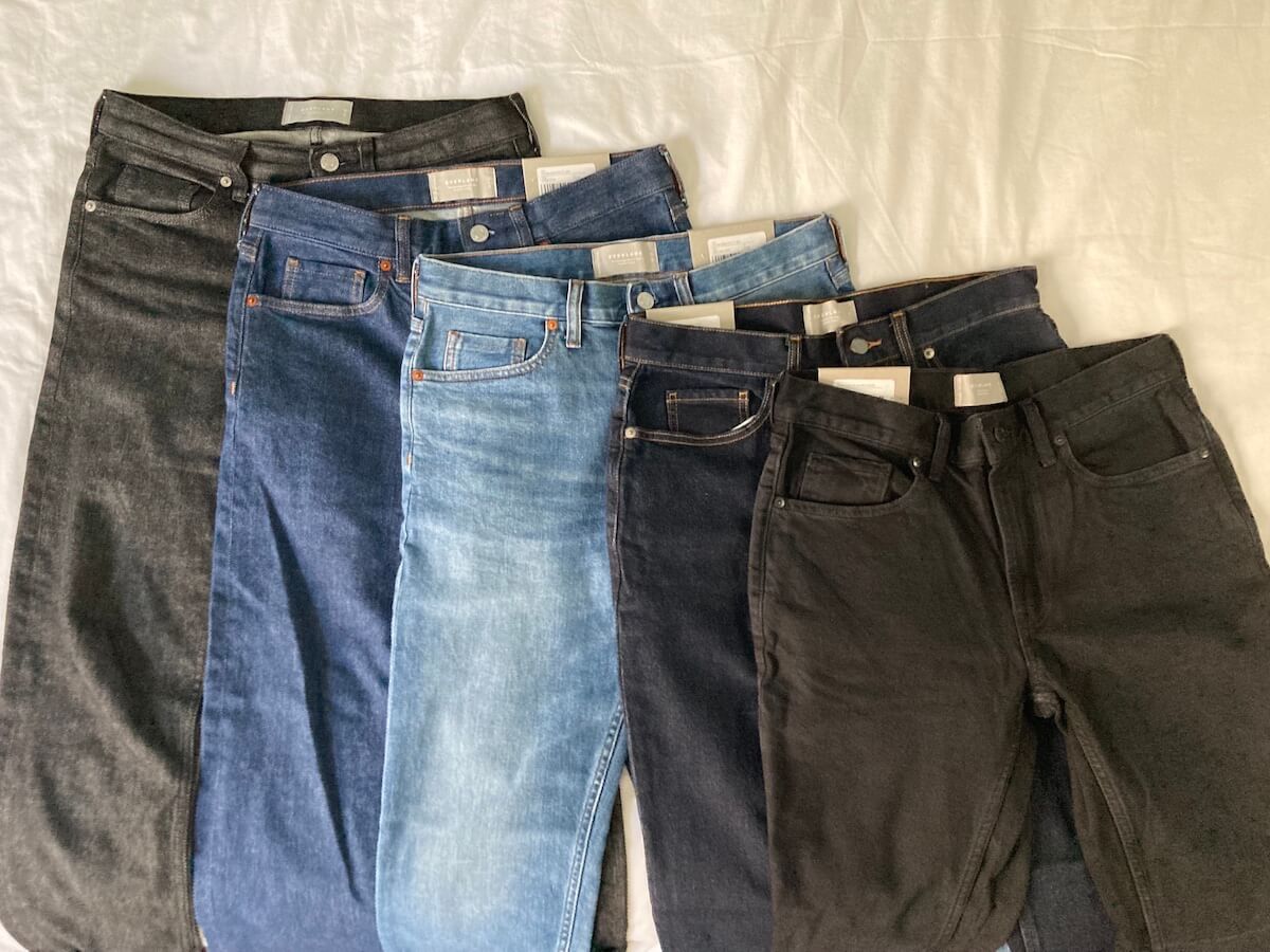 Five pairs of Everlane slim fit jeans in different washes, laid out on a bed.