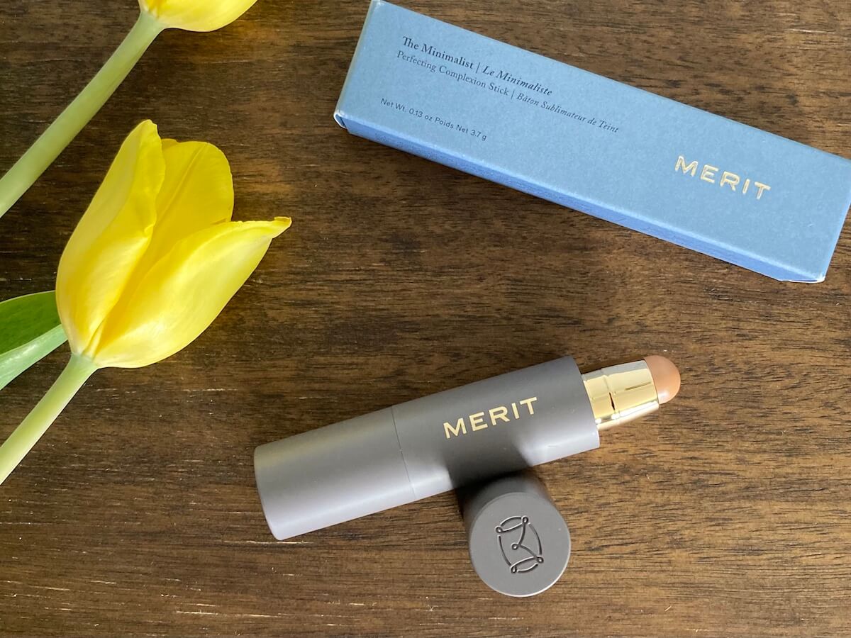 Merit The Minimalist stick opened, on a wooden surface, next to two daffodils.