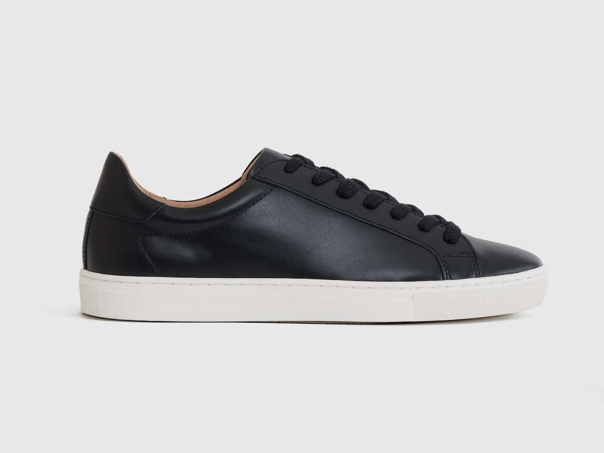 A product photo of a black leather low-profile sneaker.