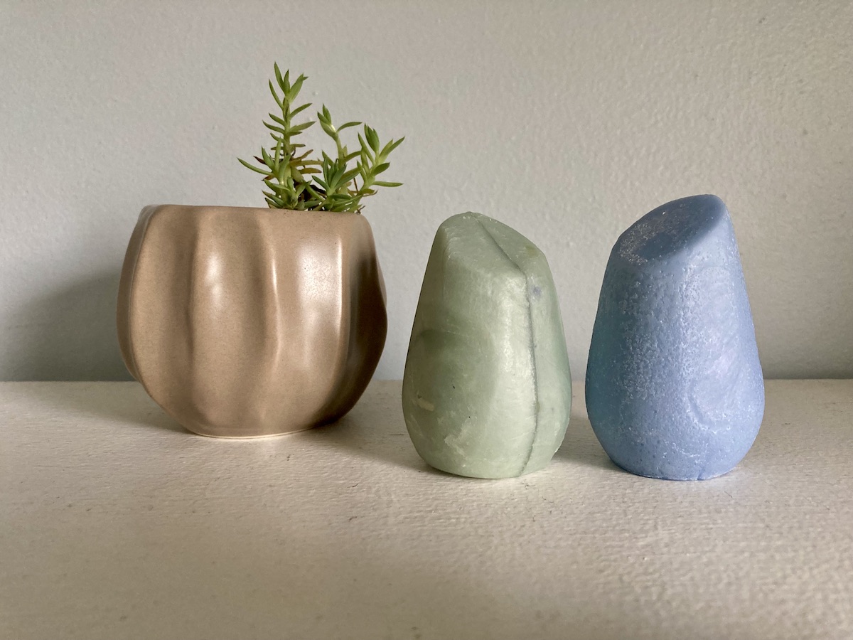 Two bar shampoos that look like little sculptures next to a small potted plant.