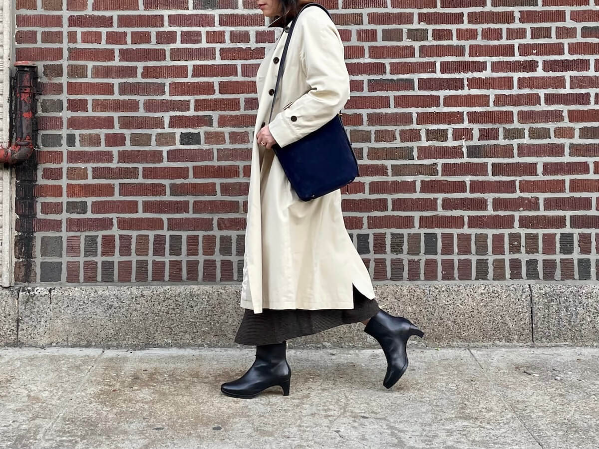 A person walks in front of a red brick wall in a beige trench coat.