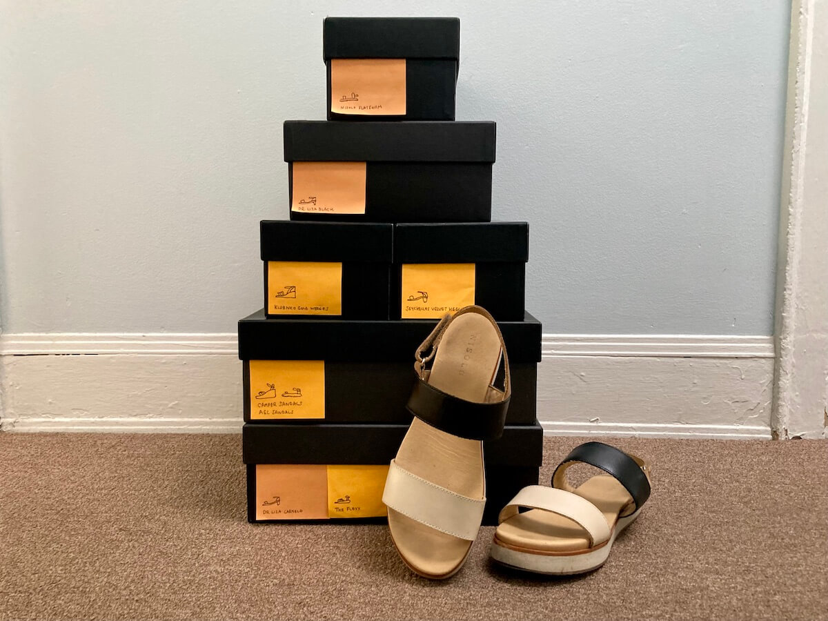 A stack of boxes with post-it notes that have drawings of the shoes inside of them, plus a pair of sandals
