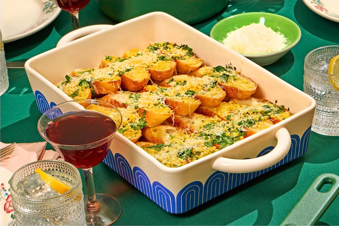 Product photo of a ceramic dish with a retro pattern on a green table with glasses and plates. There is garlic bread in the dish.