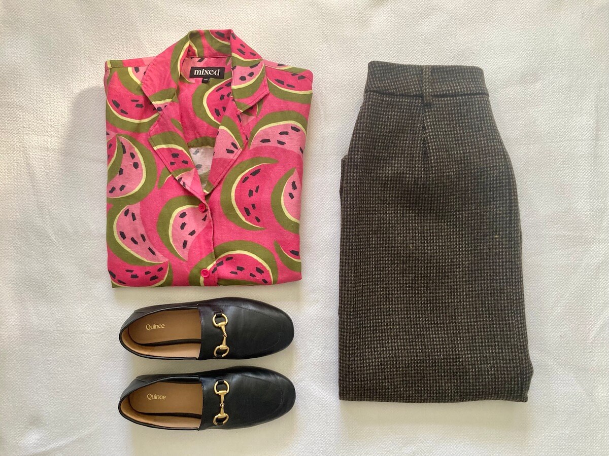A flat lay of a watermelon print shirt, a checkered wool skirt, and horsebit loafers.